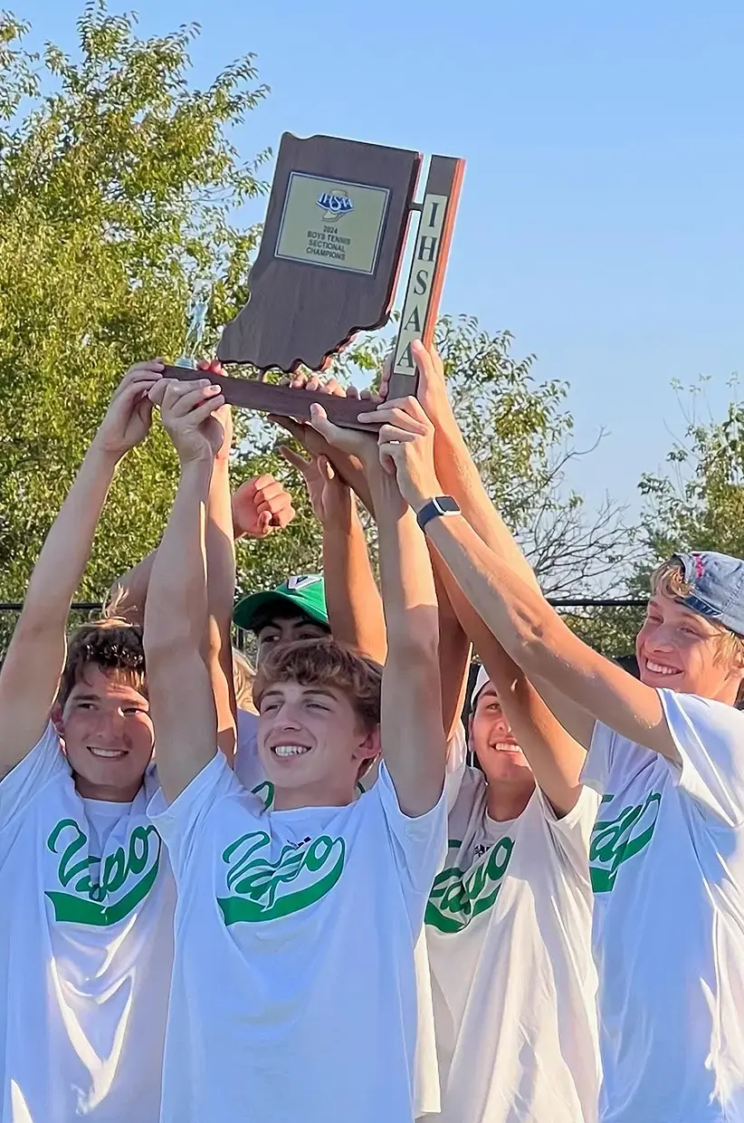 A group of Valparaiso High School young men, including Mitchell, joyfully lift the 2024 boys tennis sectional championship trophy. They are outdoors with trees in the background.